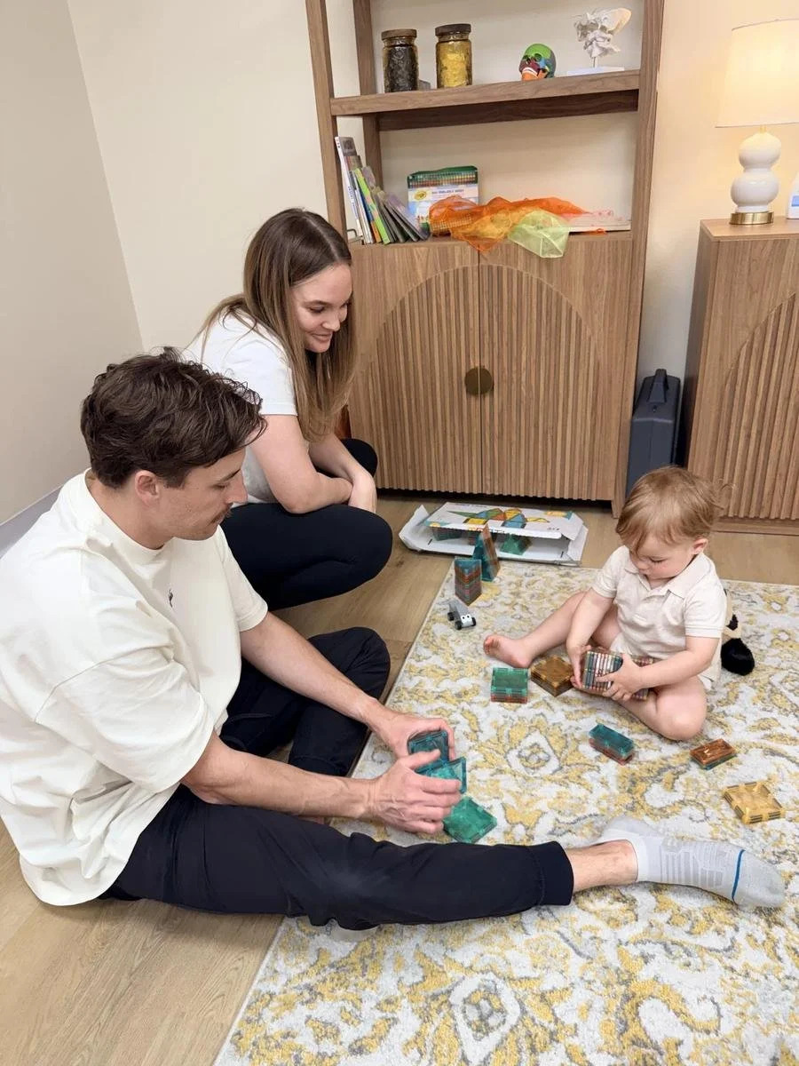 Two adults playing with a toddler in the Taproot Chiropractic kids' area
