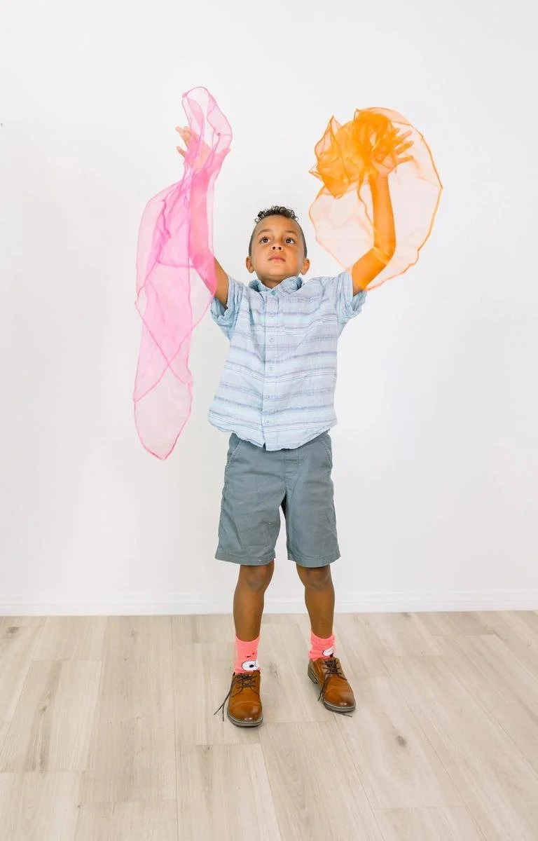 Young boy raising colorful sensory scarves overhead