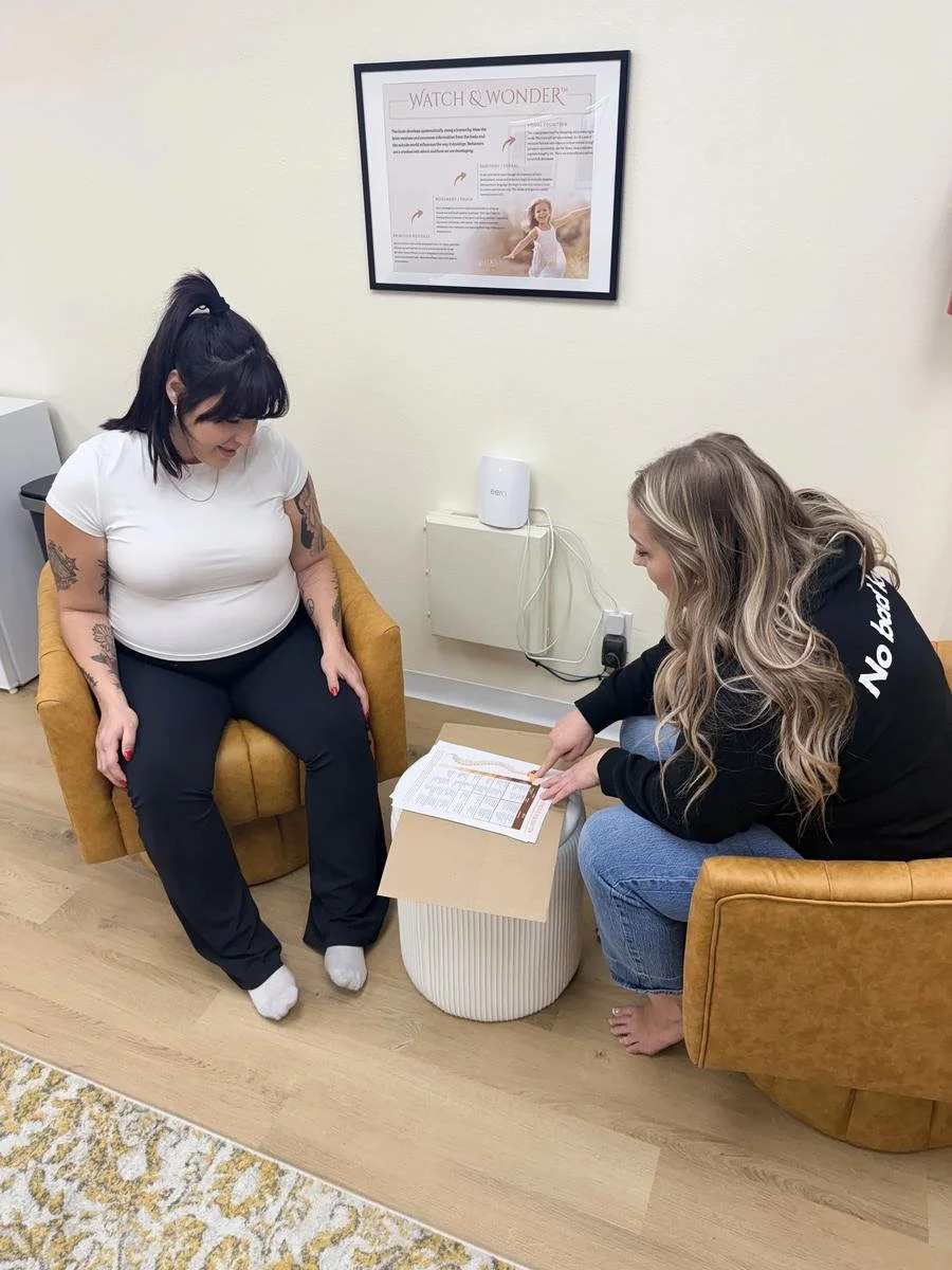 Dr. Jennifer Gordon kneeling to explain a spinal chart to a pregnant woman seated in a yellow armchair