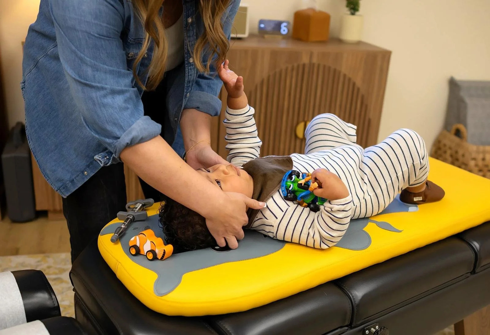 Chiropractor gently supporting a toddler’s neck while the child lies on a pediatric treatment table