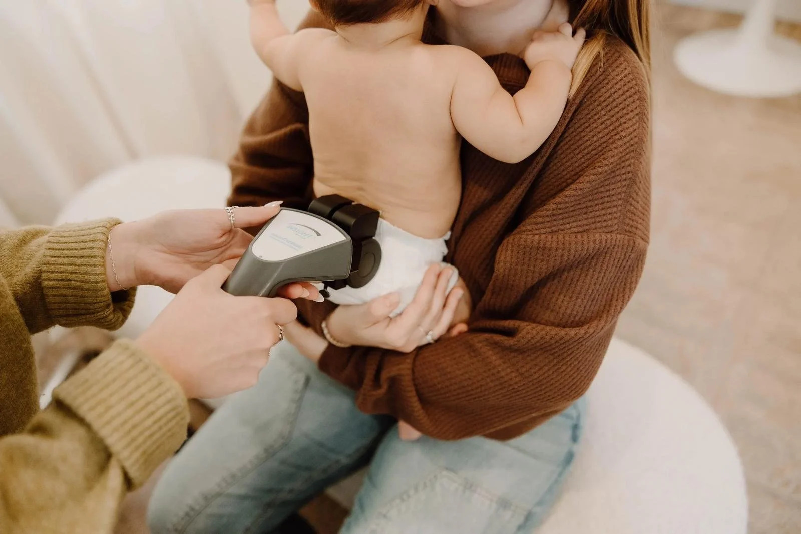 Chiropractor using a handheld scanning device on an infant’s lower back while the baby is held by a parent.