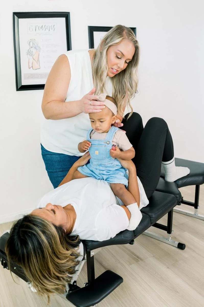 Dr. Jennifer Gordon gently supporting a toddler seated on a parent