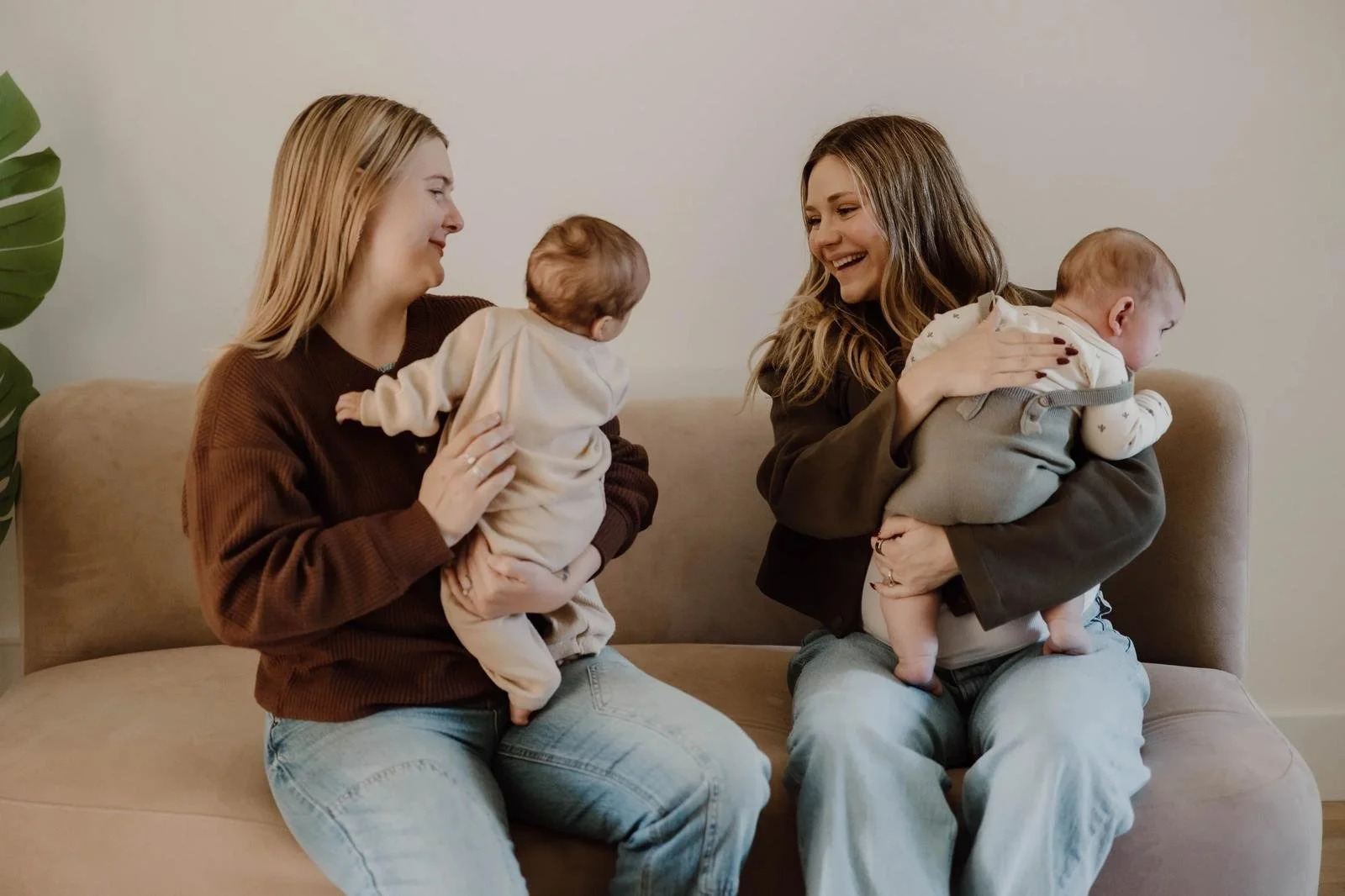Two mothers sitting together on a couch holding babies