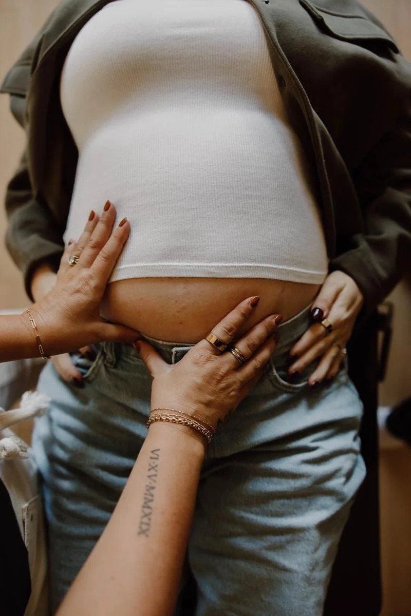 Close-up of hands placed gently on a pregnant patient's lower abdomen