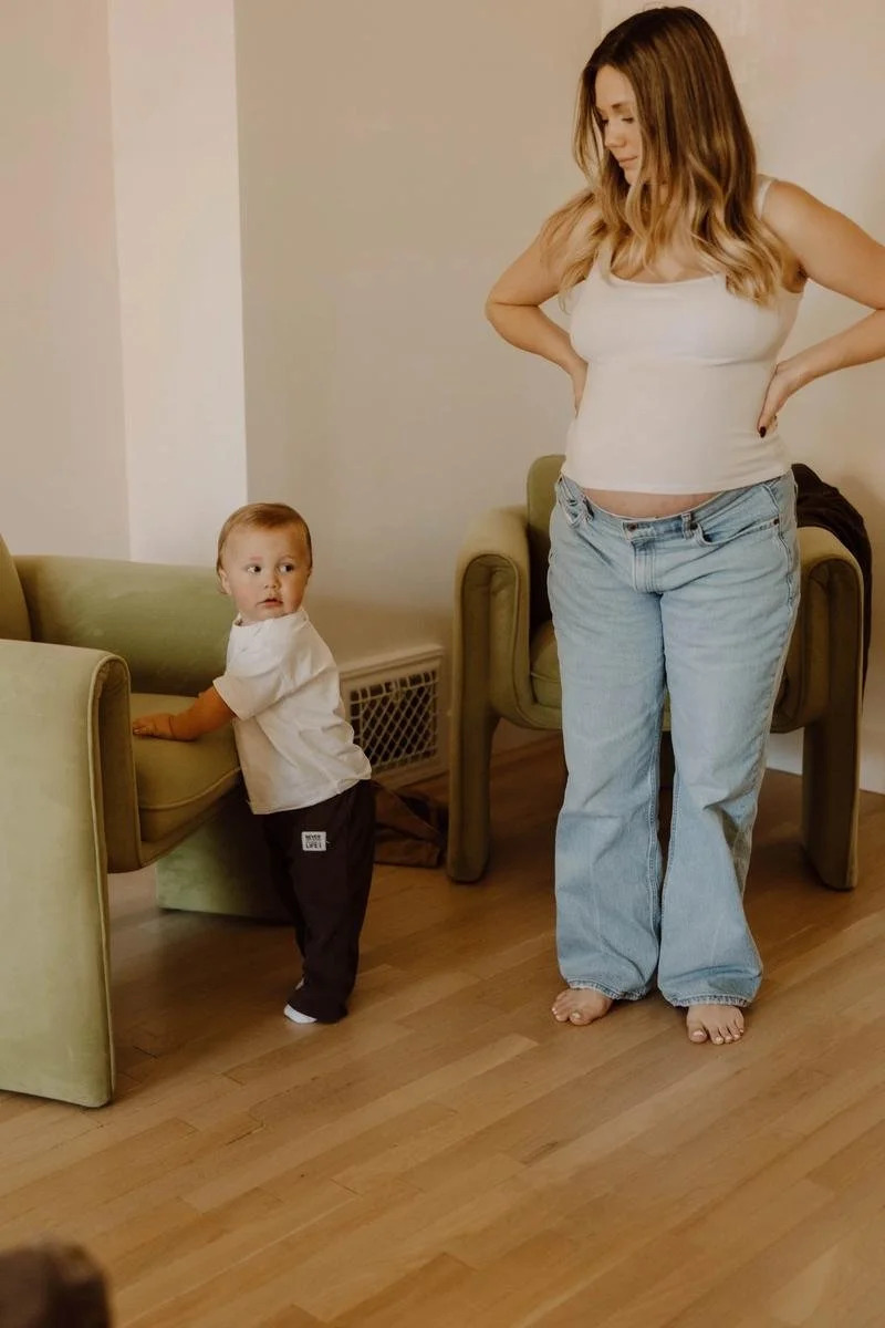 A pregnant patient standing with hands on her hips while a toddler plays nearby