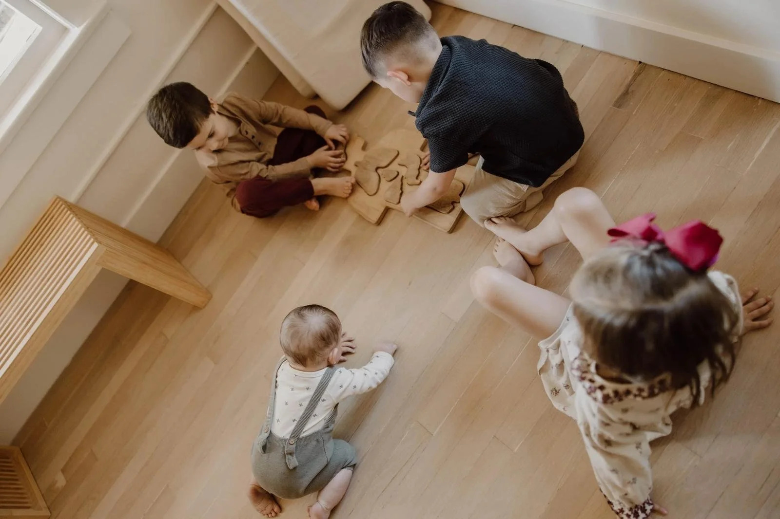 Three children play with a wooden puzzle while an infant crawls toward them