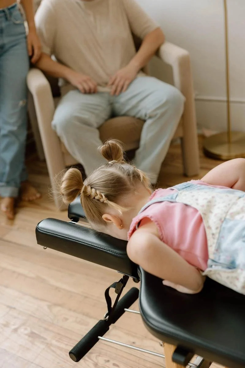 Toddler resting face down on a treatment table while two adults wait in the background